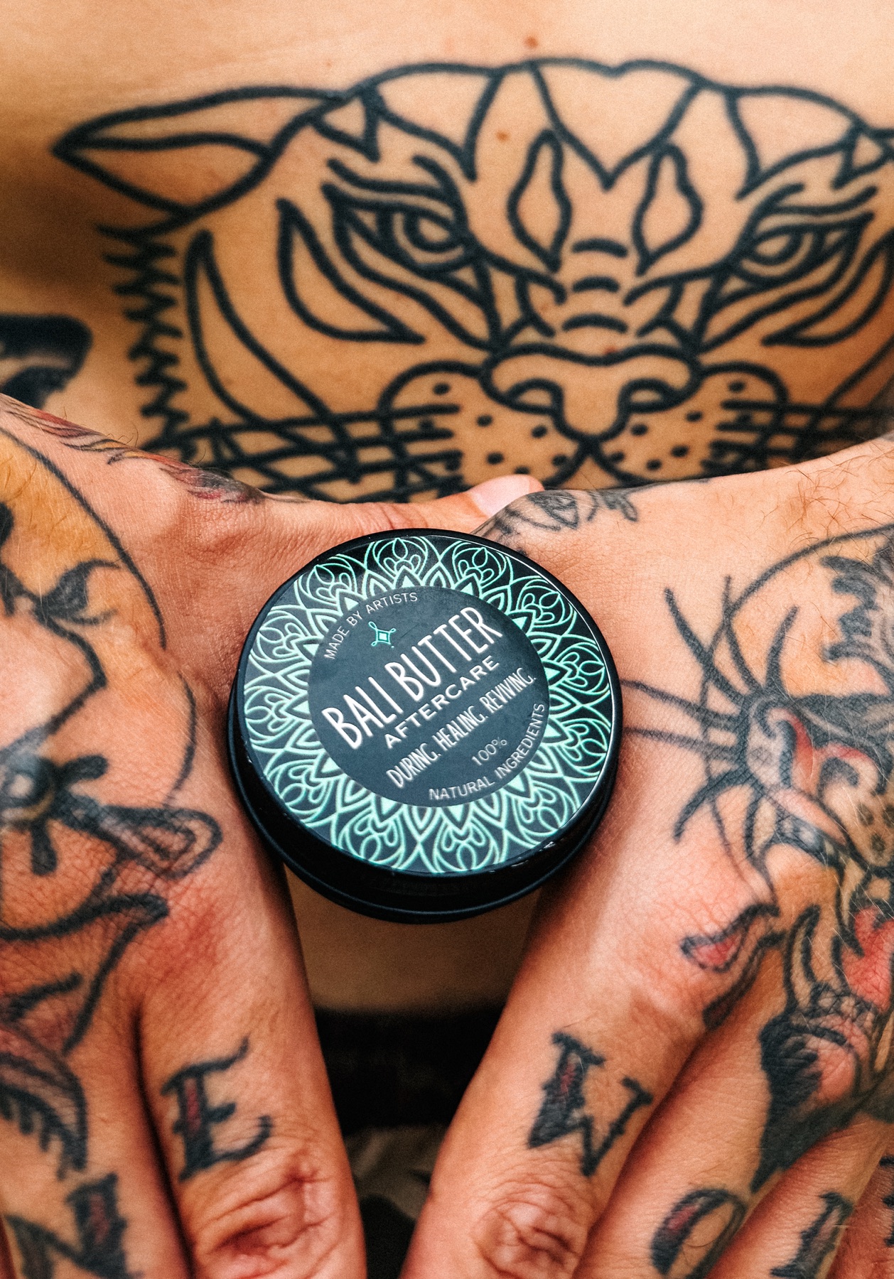 Bali Butter tattoo aftercare tin held by tattooed hands